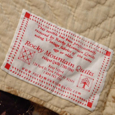 Image of the Rocky Mountain Quilts Label. Reads: This textile has been professionally restored by Rocky Mountain Quilts using Vintage fabrics of the same age or older. Rocky Mountain Quilts Antique Quilts 1780 - 1940 Betsey Telford 130 York St York Village, ME 03909 1-800-762-5914 www.rockymountainquilts.com