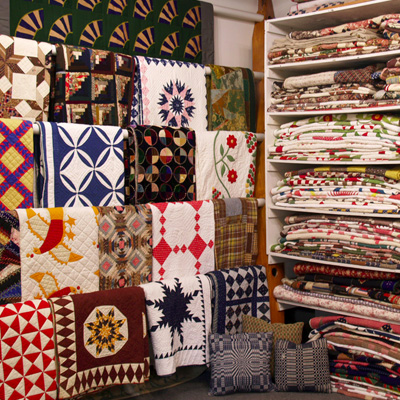Image of the interior of Rocky Mountain Quilts, showing quilts hanging on racks in the left third of the picture, and quilts neatly folded on shelves in the right two thirds of the picture.