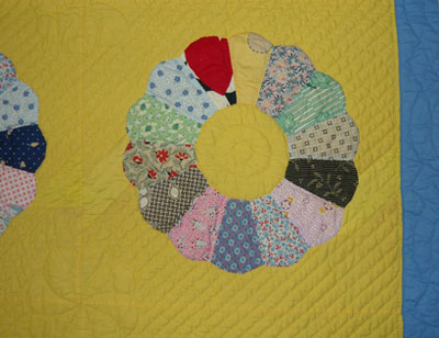 A picture of a quilt after the restoration process. Shows a yellow quilt with the tears fixed, and a replacement piece of appliqué